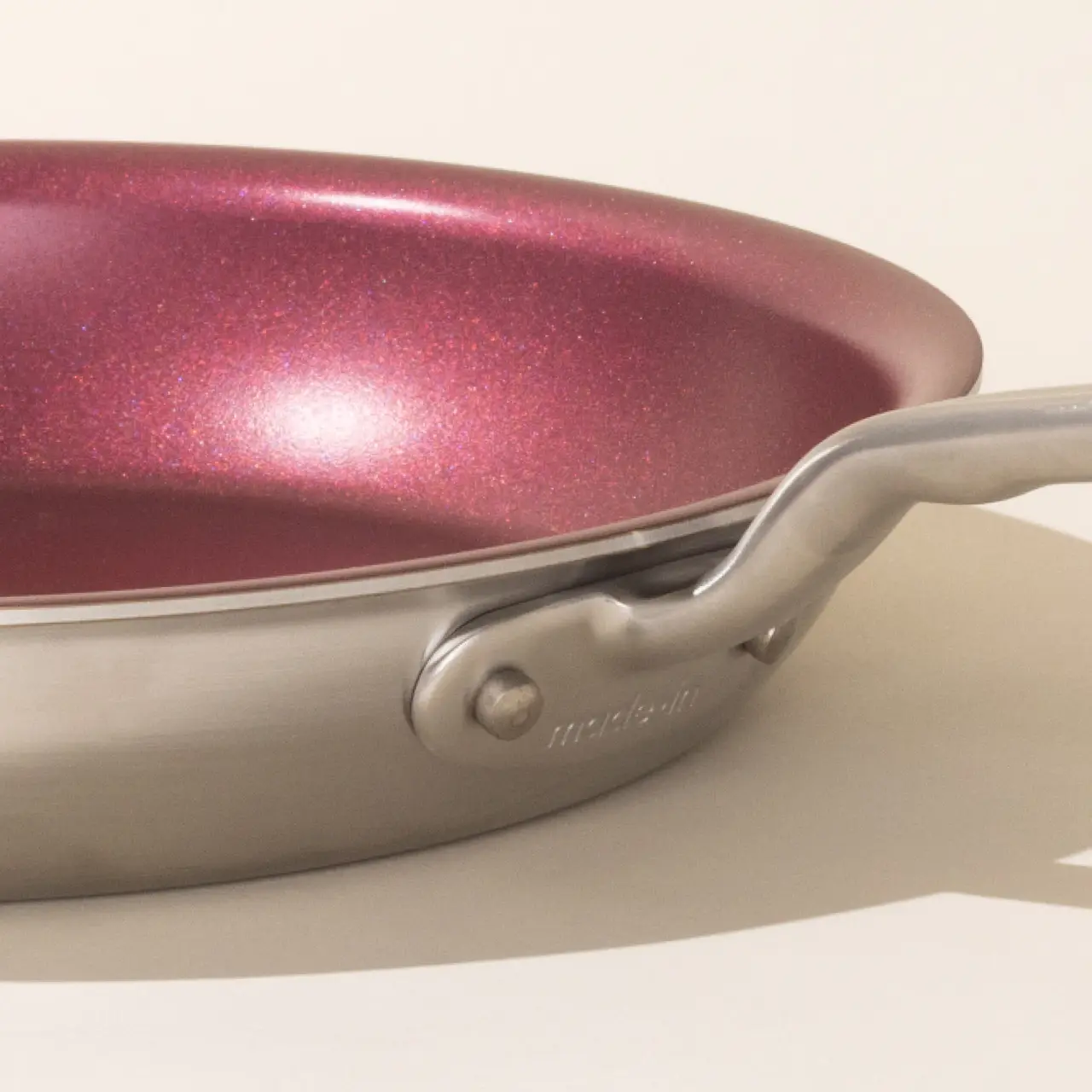 A close-up of a metallic frying pan with a red-hued interior and a riveted handle.