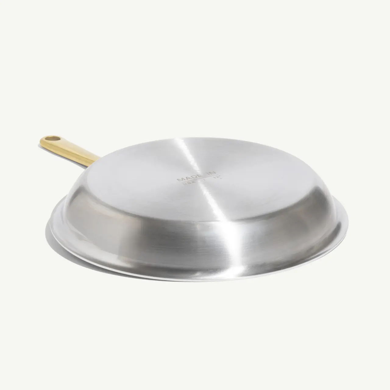 A stainless steel skillet with a wooden handle rests on a light background.