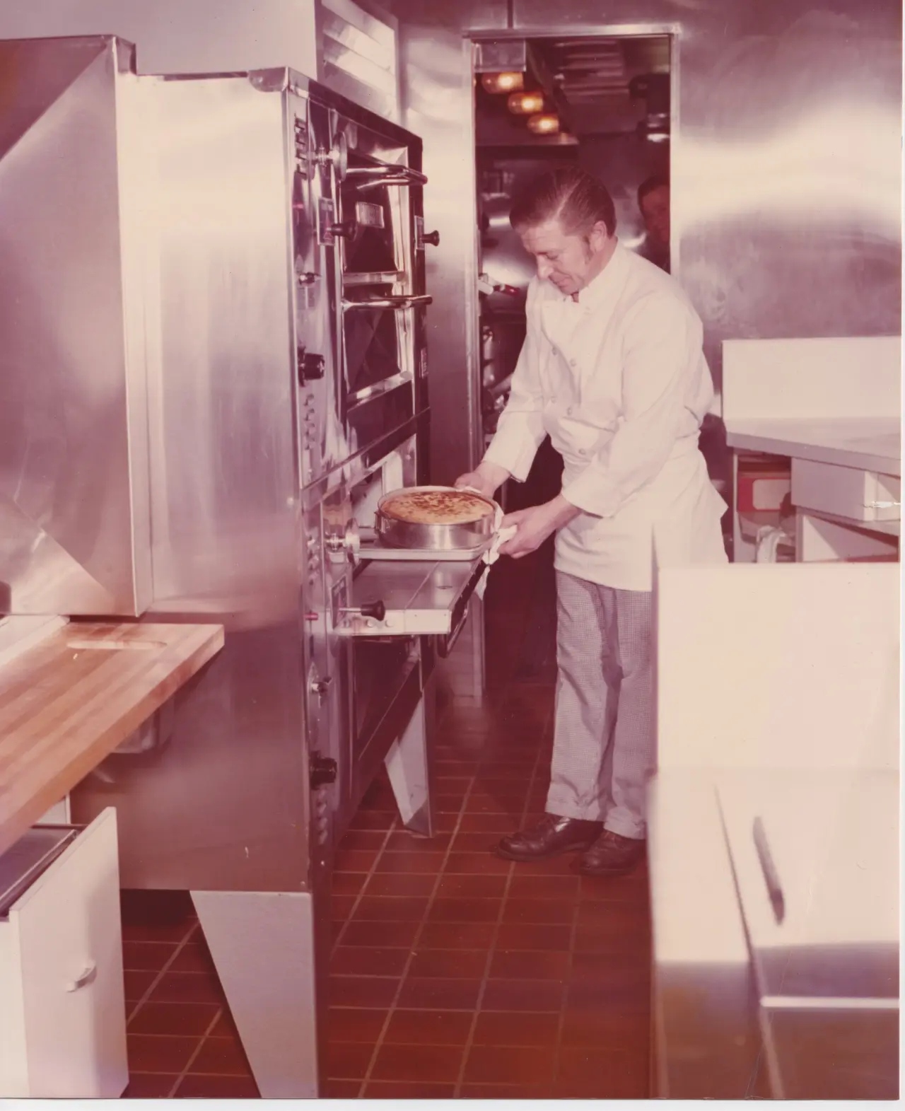 A chef is carefully removing a pie from an industrial oven in a professional kitchen setting.