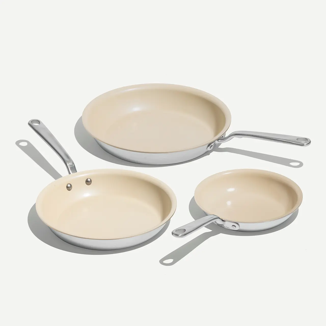 Three cream-colored frying pans of different sizes are placed on a white background.