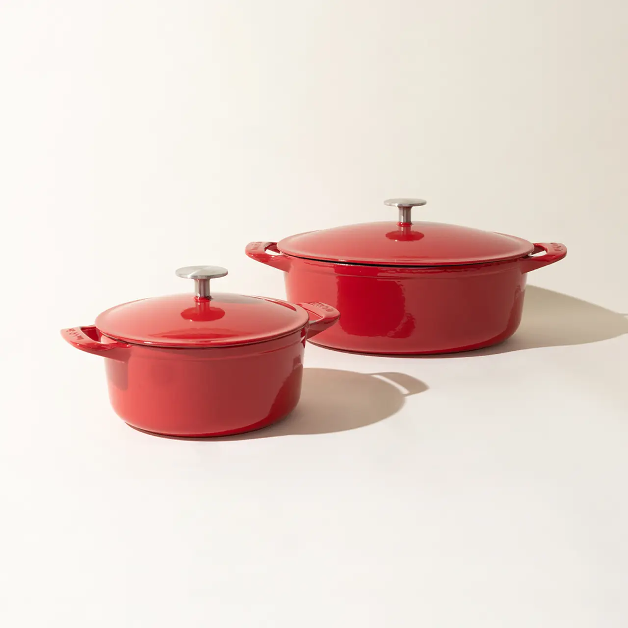 Two red enameled pots with lids on a light background.