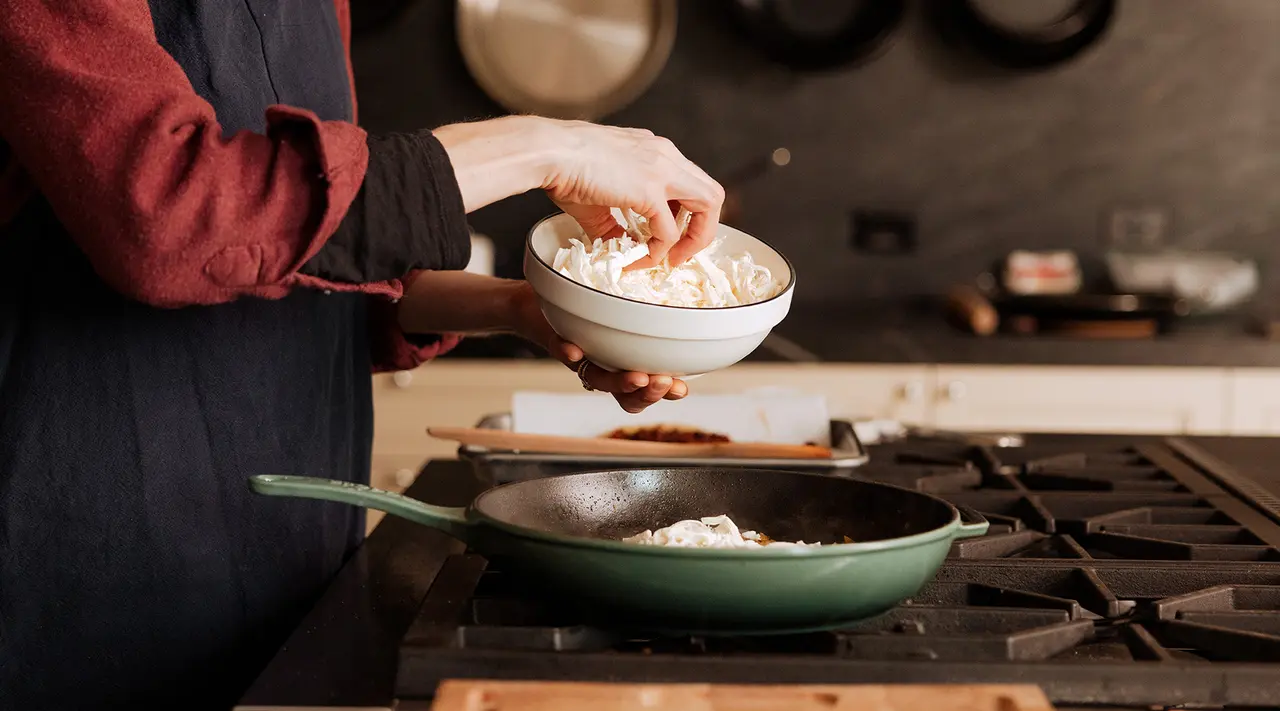 A person is adding ingredients to a pan on the stove, indicating they are in the process of cooking.