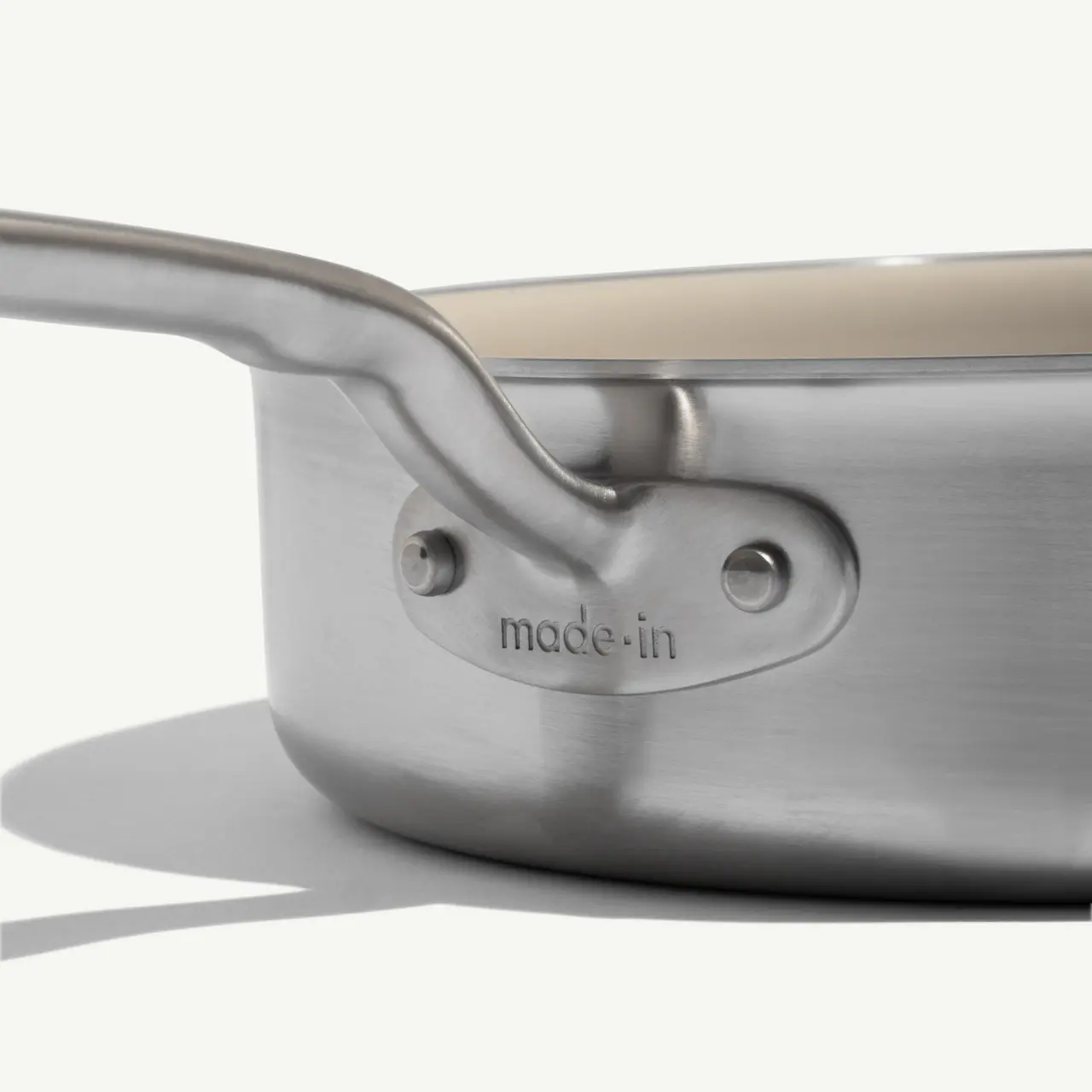 A close-up view of a stainless steel frying pan with a sleek handle and a "made-in" logo on the side.
