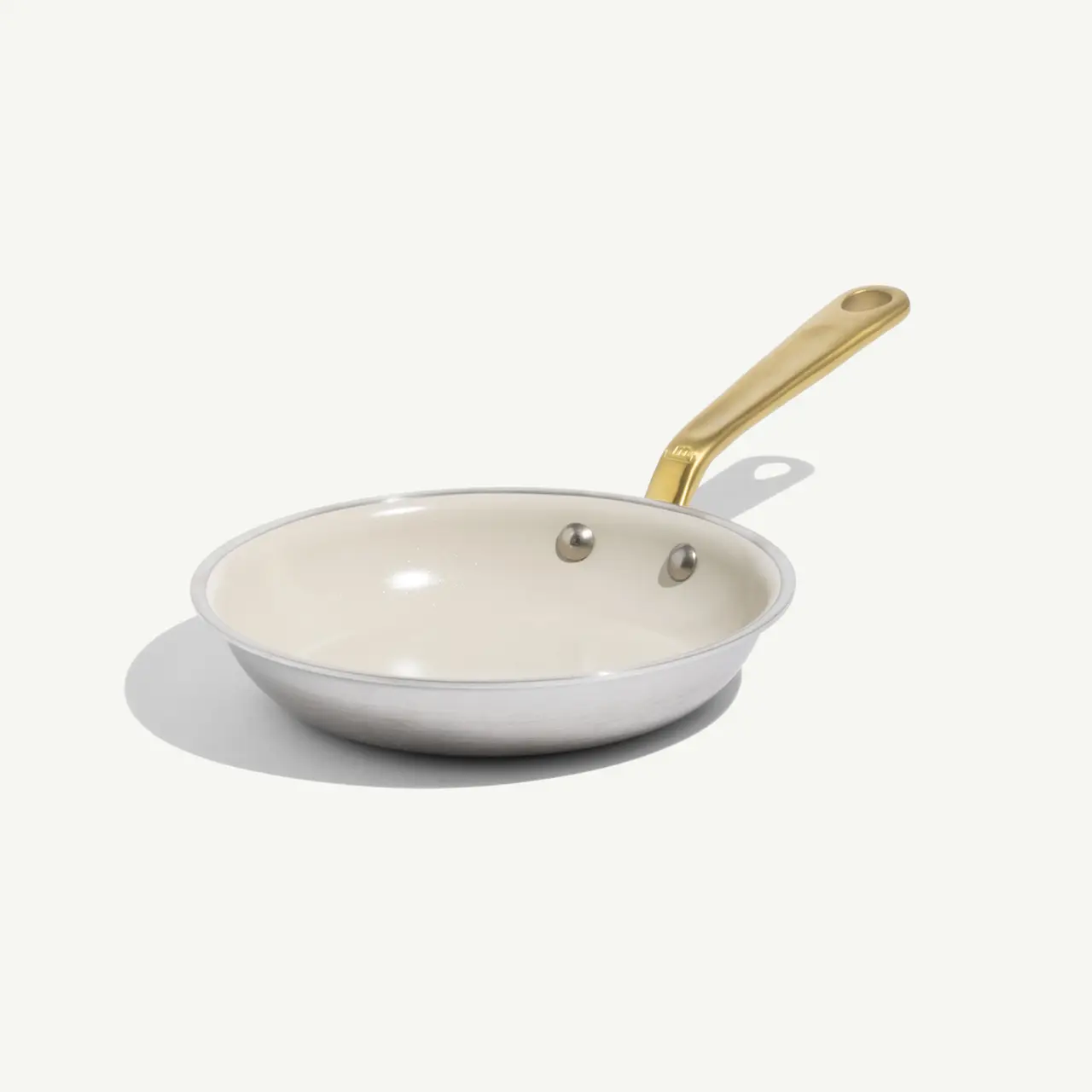 A non-stick frying pan with a cream-colored interior and a gold handle.