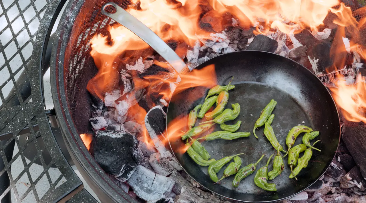 A skillet with sliced bell peppers is being cooked over an open flame on a grill.