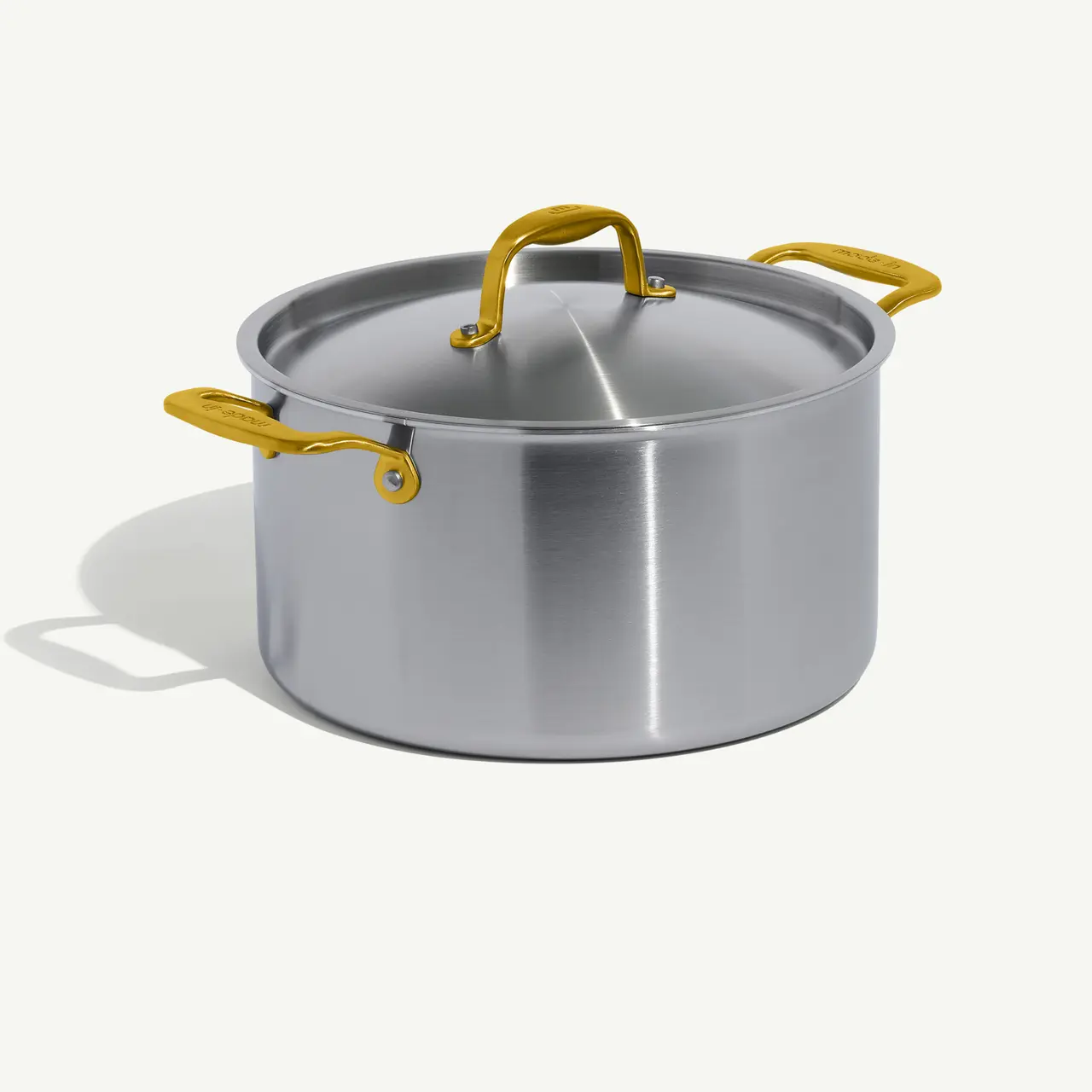 A stainless steel pot with a matching lid and yellow handles rests on a light background.