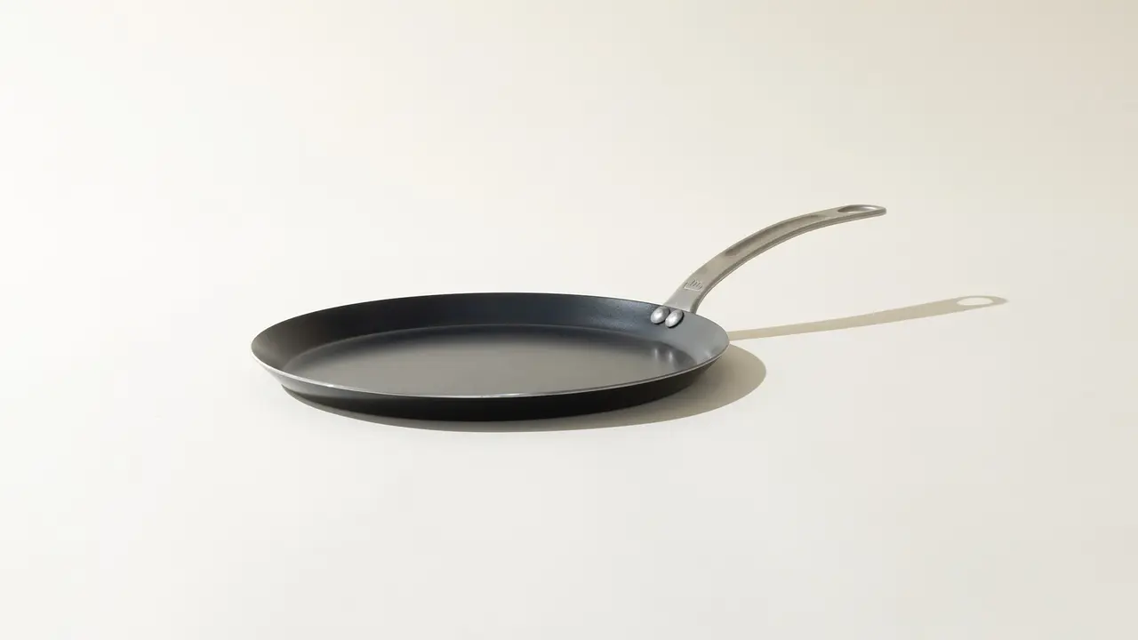 A non-stick frying pan with a stainless steel handle is positioned against a light background.