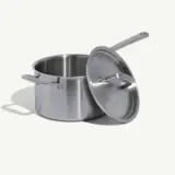 A stainless steel pot with a lid leaning against its side.