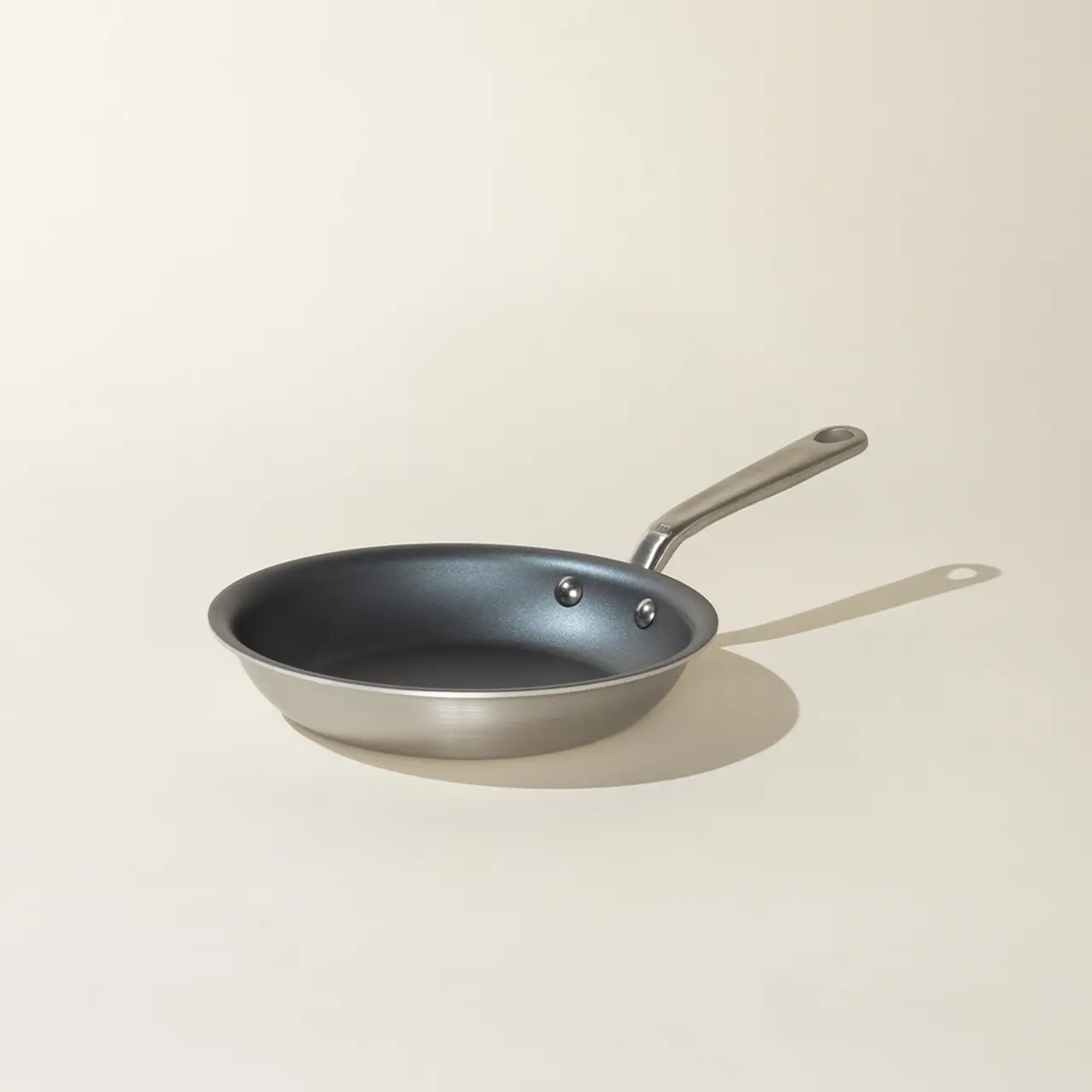 A stainless steel frying pan with a non-stick coating is casting a shadow on a light surface.