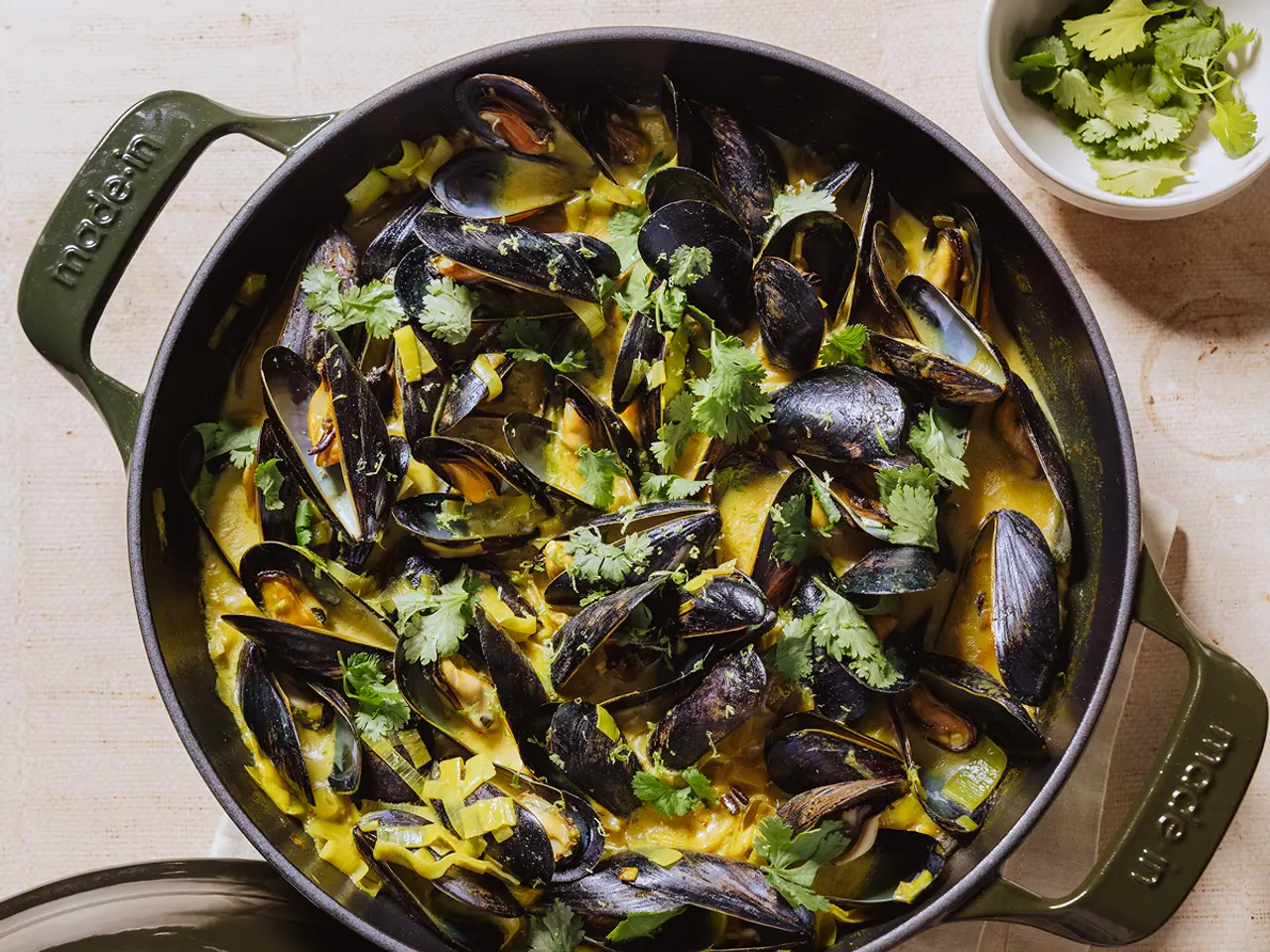 A deep green pot filled with mussels garnished with fresh cilantro and spices.