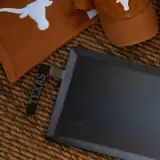 A brown hat and towel featuring a white longhorn logo, along with a black cutting board labeled "TEXAS," are arranged on a textured surface.
