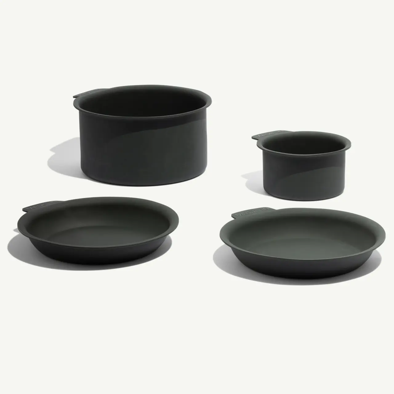 Four dark green cooking pots and plates of varying sizes are displayed on a light background.