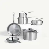 A collection of stainless steel cookware, including pots and pans, arranged on a light background.
