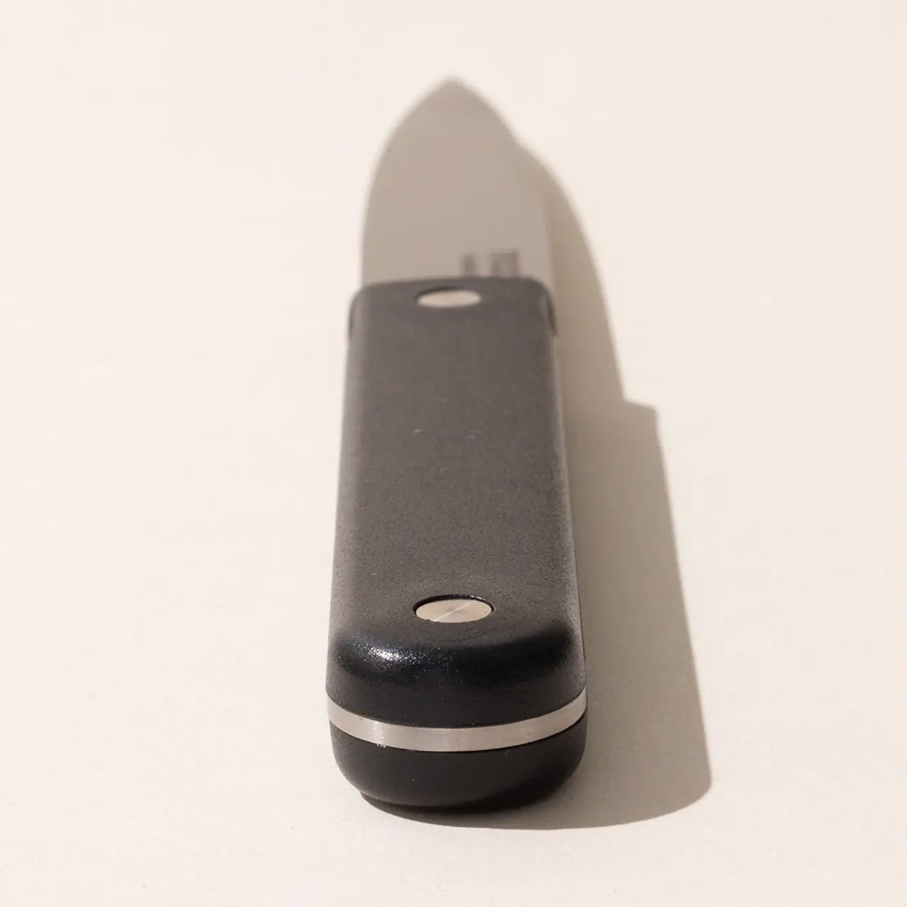 A folding pocket knife with a black handle is partially opened on a light background.