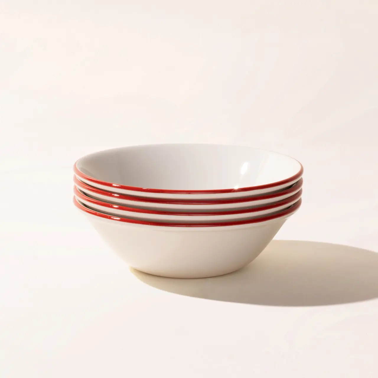 A stack of white bowls with red stripes sits on a light surface against a neutral background.