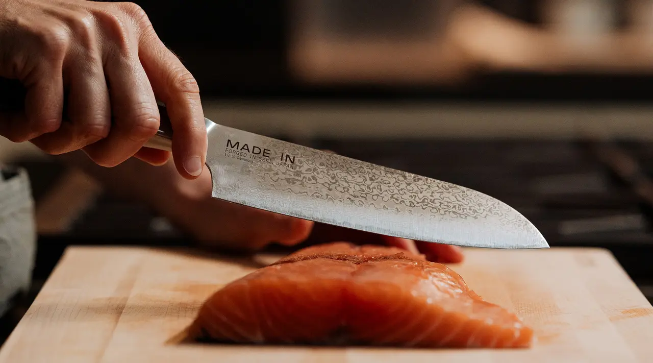 A person's hand is slicing salmon on a wooden board with a finely crafted knife.