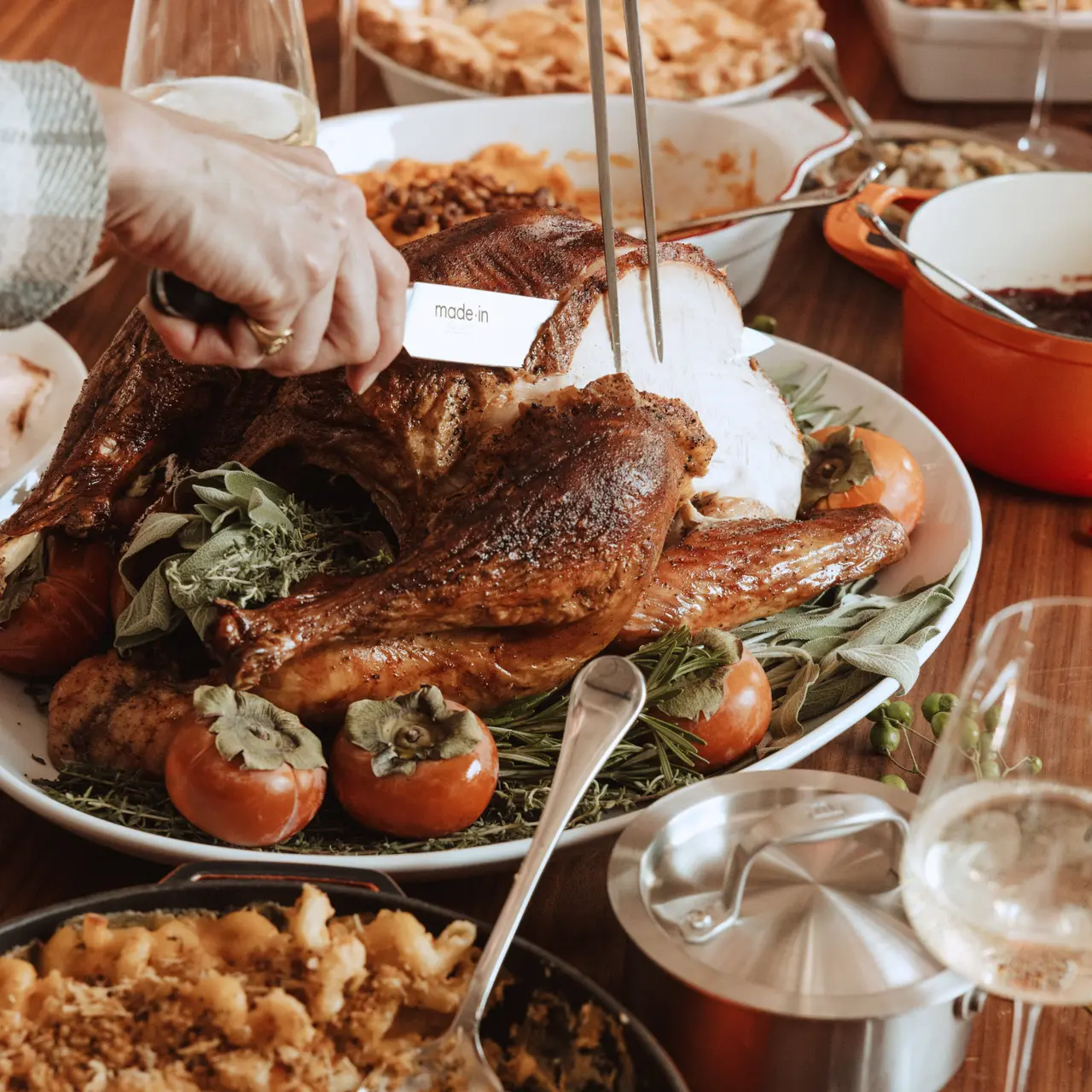 A hand is carving a beautifully roasted turkey surrounded by sides and garnishes on a festive dining table.