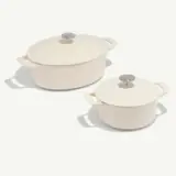 Two cream-colored covered casserole dishes of different sizes with handles and stainless steel knobs are shown on a plain background.