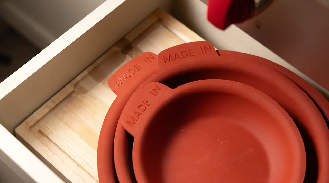 Close-up of red rubber bowls with "MADE IN" embossed on the edge, sitting inside a wooden drawer.