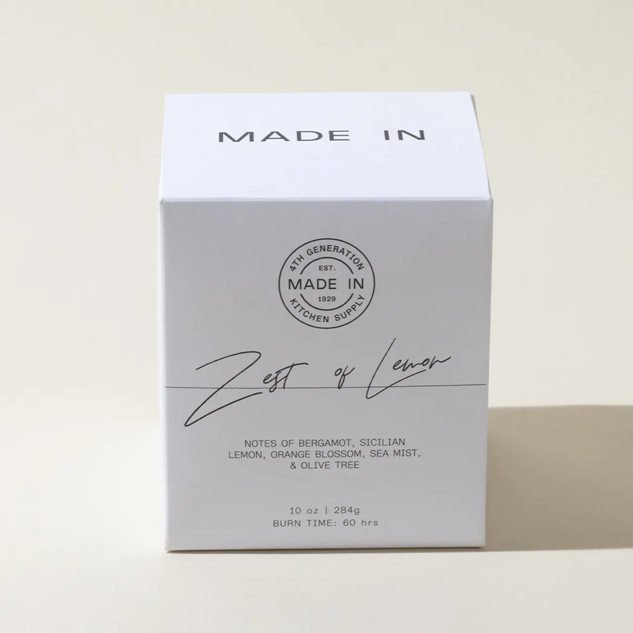 A minimalist-designed candle box with text "MADE IN ___ GENERATION MADE IN ____ KITCHEN SINK" and "Zest of Lemon" featuring notes of bergamot, Sicilian lemon, and other fragrances listed.