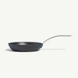A black frying pan with a long handle is positioned on a white surface.