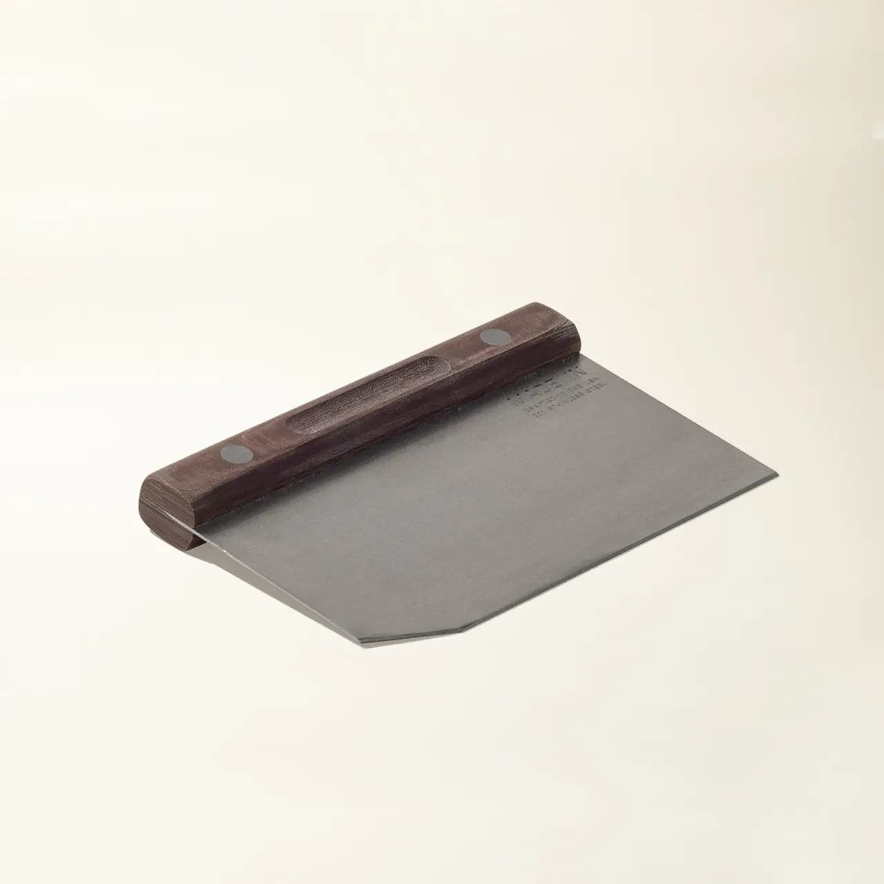 A stainless steel dough scraper with a wooden handle lies against a plain background.