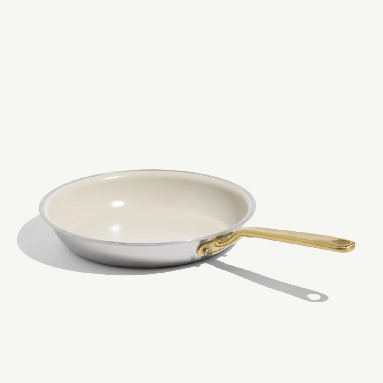 A white frying pan with a gold handle is positioned on a light surface, casting a soft shadow.