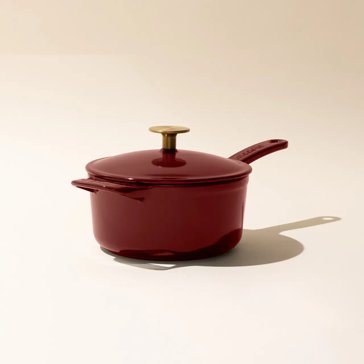 A burgundy saucepan with a gold-tone handle and a matching lid against a neutral background.