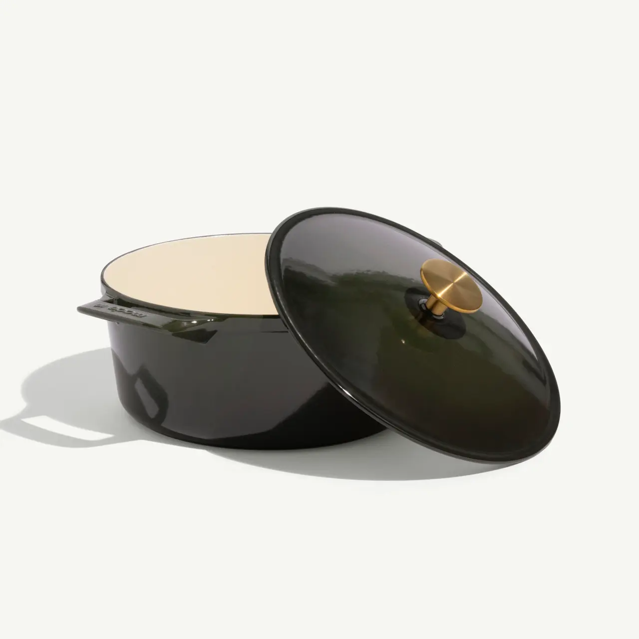 A green enameled cast iron Dutch oven with a matching lid partially open, showcasing its cream-colored interior.