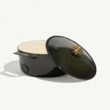 A green enameled cast iron Dutch oven with a matching lid partially open, showcasing its cream-colored interior.