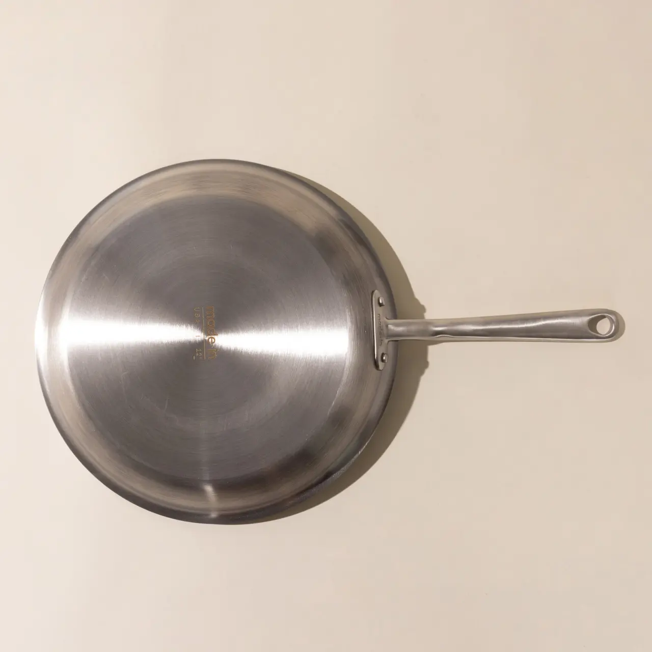 A stainless steel frying pan with a long handle is displayed against a neutral background.
