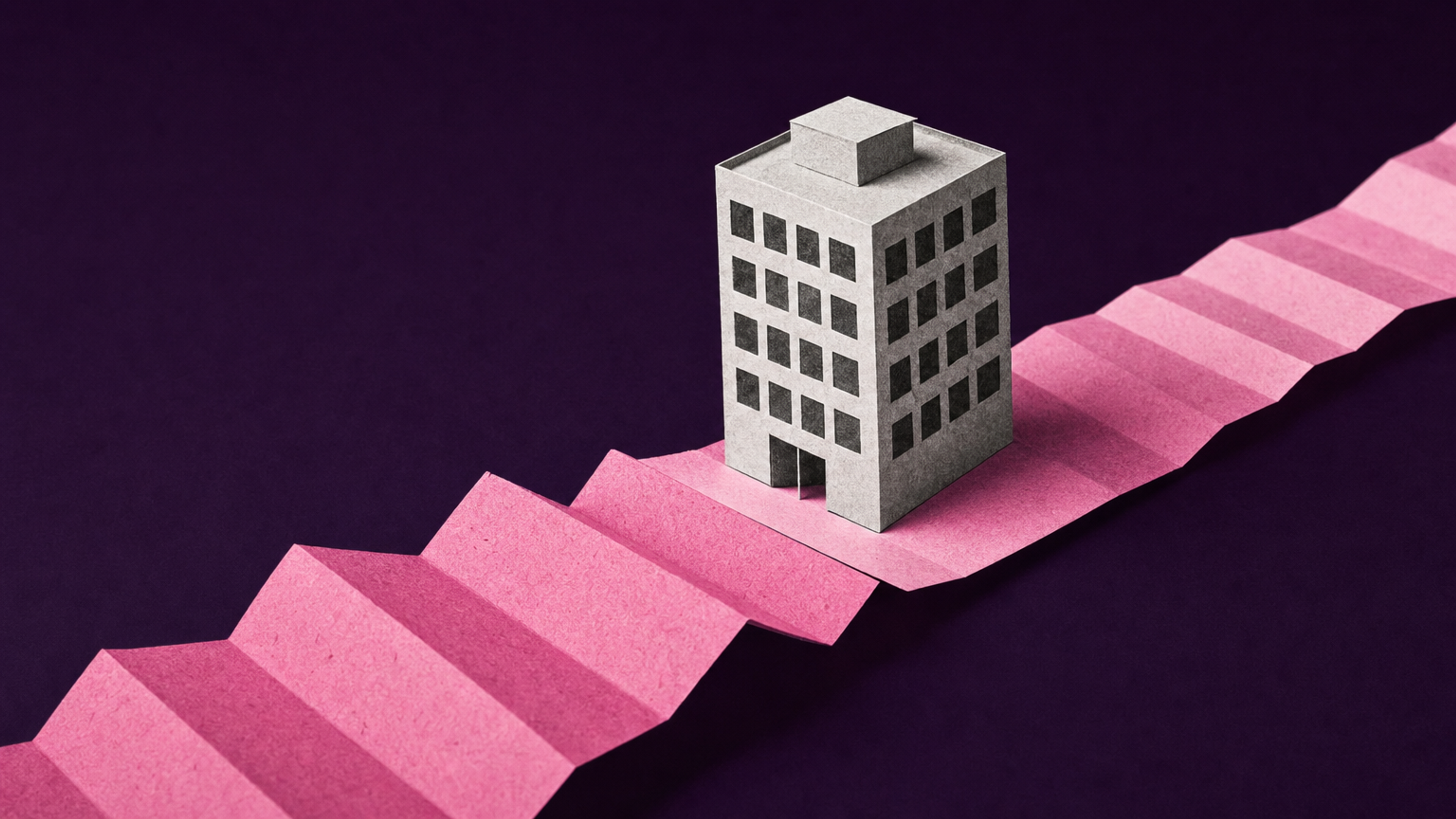 A small paper office building resting on one folded segment of a long pink paper strip that continues past both edges of the frame