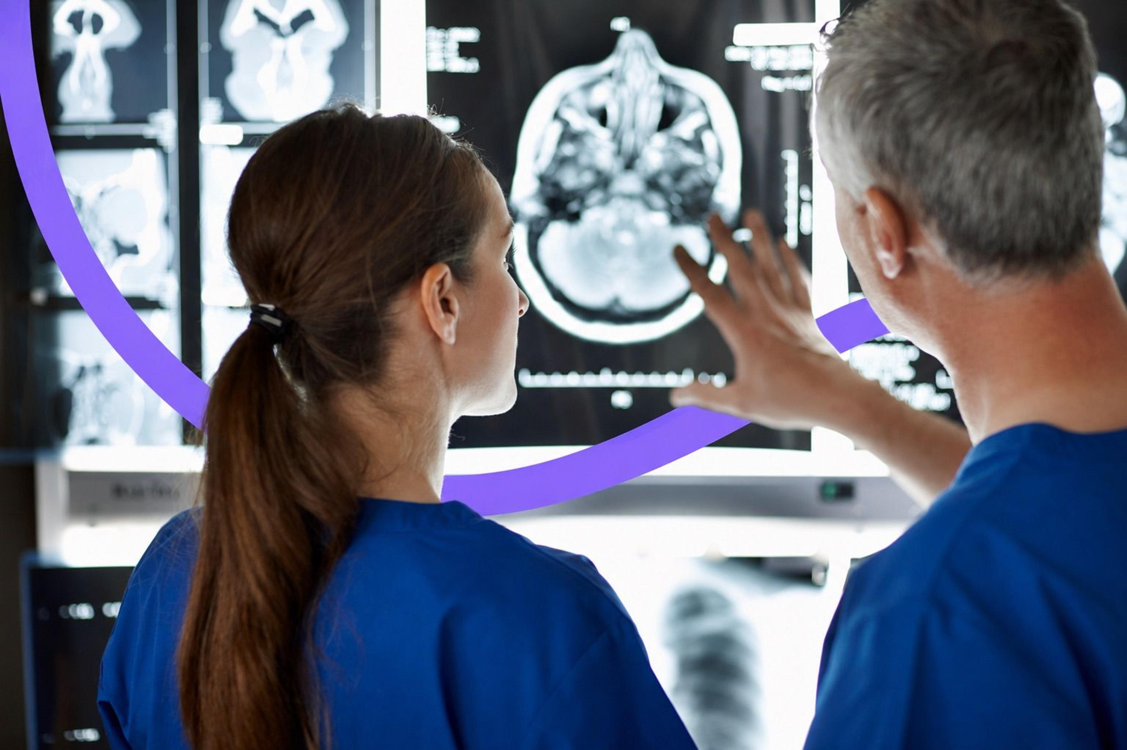 Two medical imaging technologists reviewing CT and X-ray scans on a display