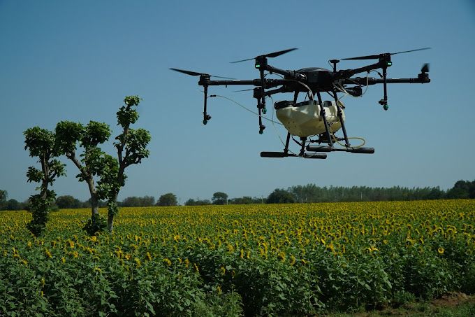 The image shows a Marut drone, a multi-rotor UAV with a sleek black frame, equipped with four propellers and various sensors and attachments. The drone hovers against a blurred outdoor background, suggesting it is in flight. The logo "Marut Drones" appears in bold text to the right, with the "A" stylized to include a red dot.