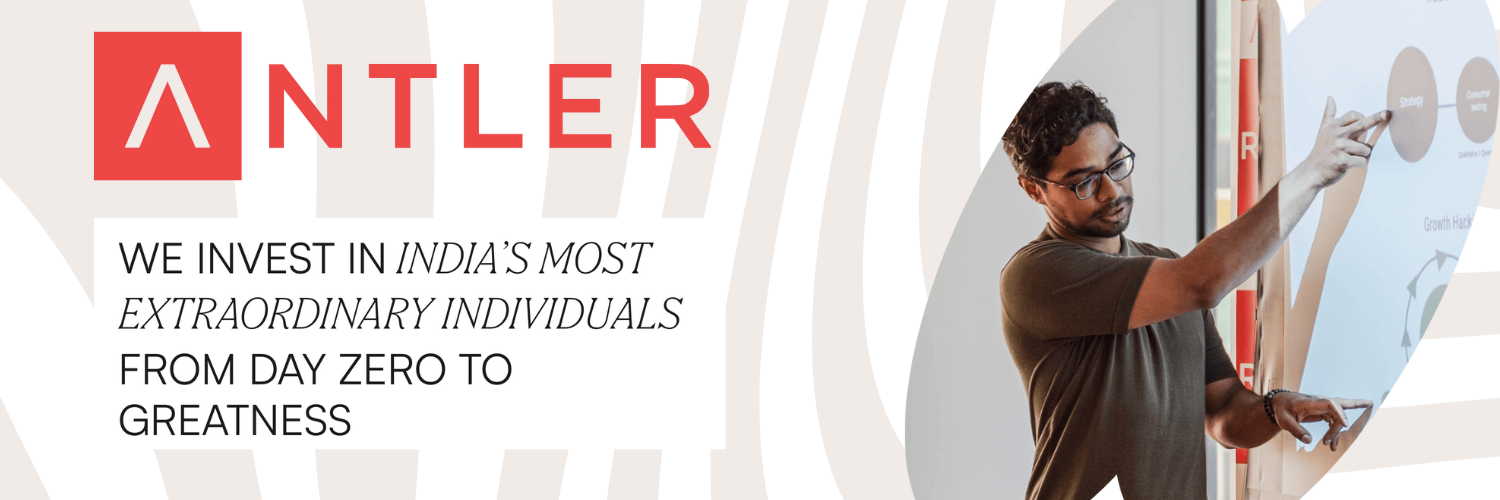 Antler India banner featuring a person presenting a strategy on a whiteboard. The Antler logo is prominently displayed on the left, with the tagline 'We invest in India's most extraordinary individuals from day zero to greatness' written below it. The background includes subtle geometric patterns.