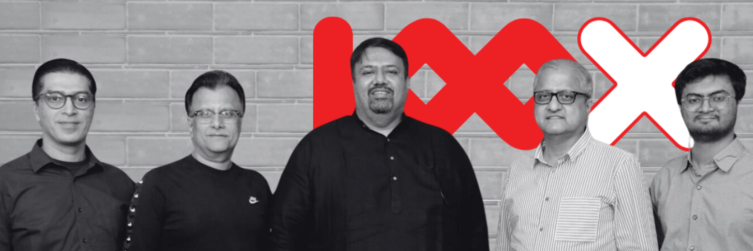 The team of 100X.VC, consisting of five men standing in front of a wall with the 100X.VC logo prominently displayed. The men are dressed in professional attire and are posing for the photo, showcasing a sense of unity and collaboration.