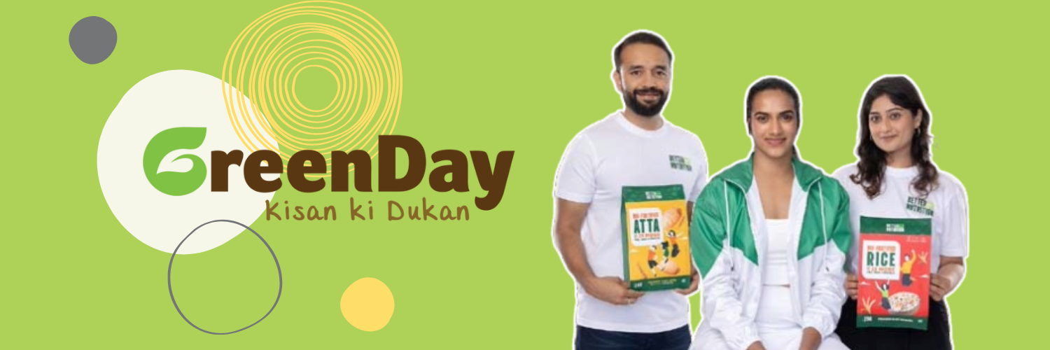 This banner image for Greenday features three people standing against a green background, with the Greenday logo and the tagline "Kisan ki Dukan". The man on the left is holding a package of 'Atta' and the woman on the right is holding a package of 'Rice', both products of Greenday. Between them stands PV Sindhu, the brand ambassador, dressed in a white shirt and green jacket, contributing to the brand's identity focused on healthier, fortified food products. The design elements in the background emphasize a fresh and organic feel, aligned with the brand's health-focused messaging.