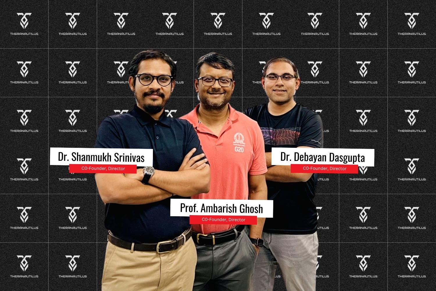 Co-founders of Theranautilus — Dr. Shanmukh Srinivas, Prof. Ambarish Ghosh, and Dr. Debayan Dasgupta — stand confidently in front of a black branded Theranautilus background. Each individual is identified with name and title labels, all dressed in casual or semi-formal attire.