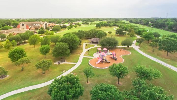 Aerial urban park with playground and asphalt trails in Houston, Texas, America. Elevated view of slides and swings in the park surrounded by green trees near Notre Dame Church