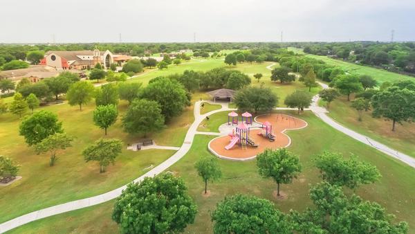 Aerial urban park with playground and asphalt trails in Houston, Texas, America. Elevated view of slides and swings in the park surrounded by green trees near Notre Dame Church