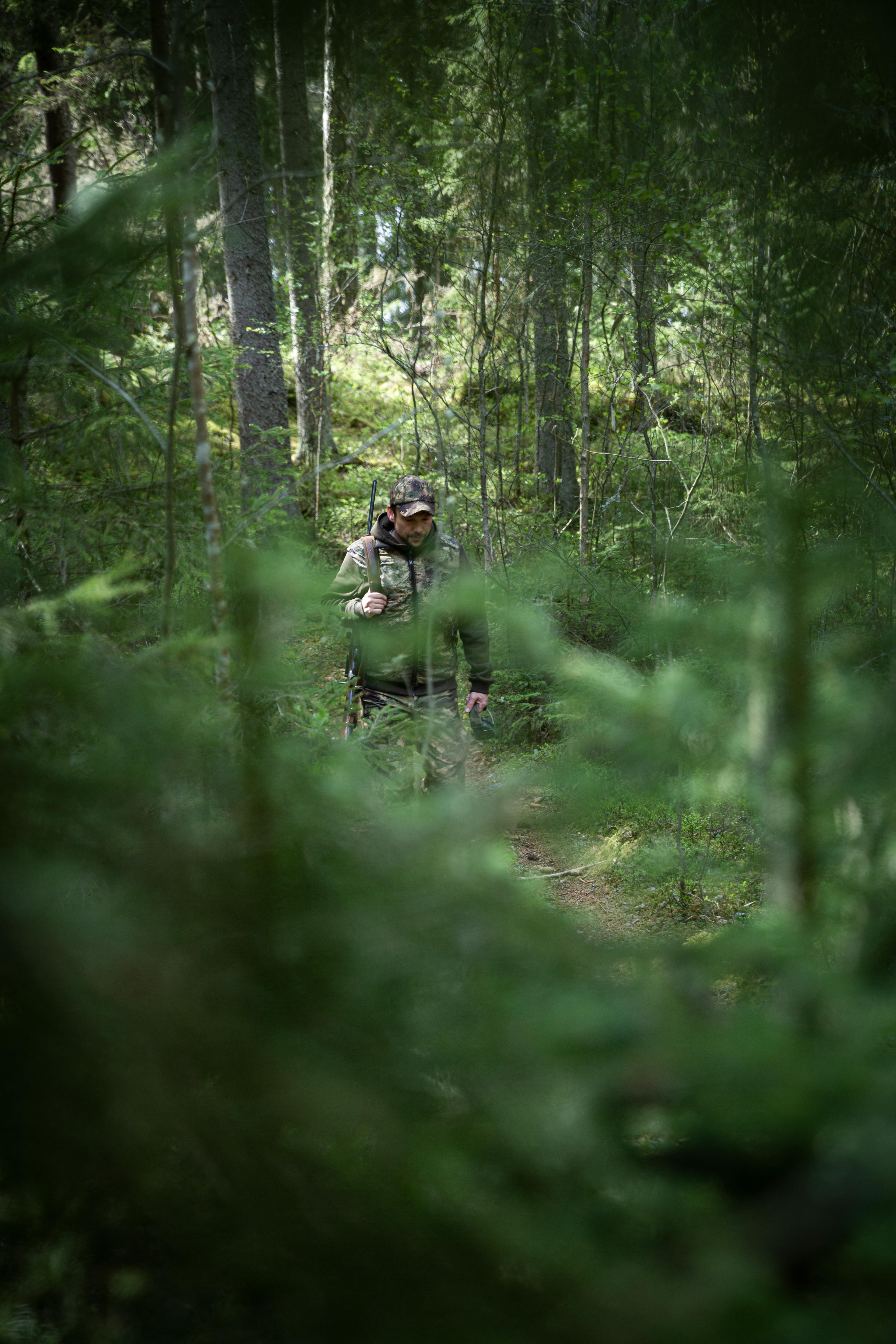 Handsome hunter man holding gun and walking in forest. American