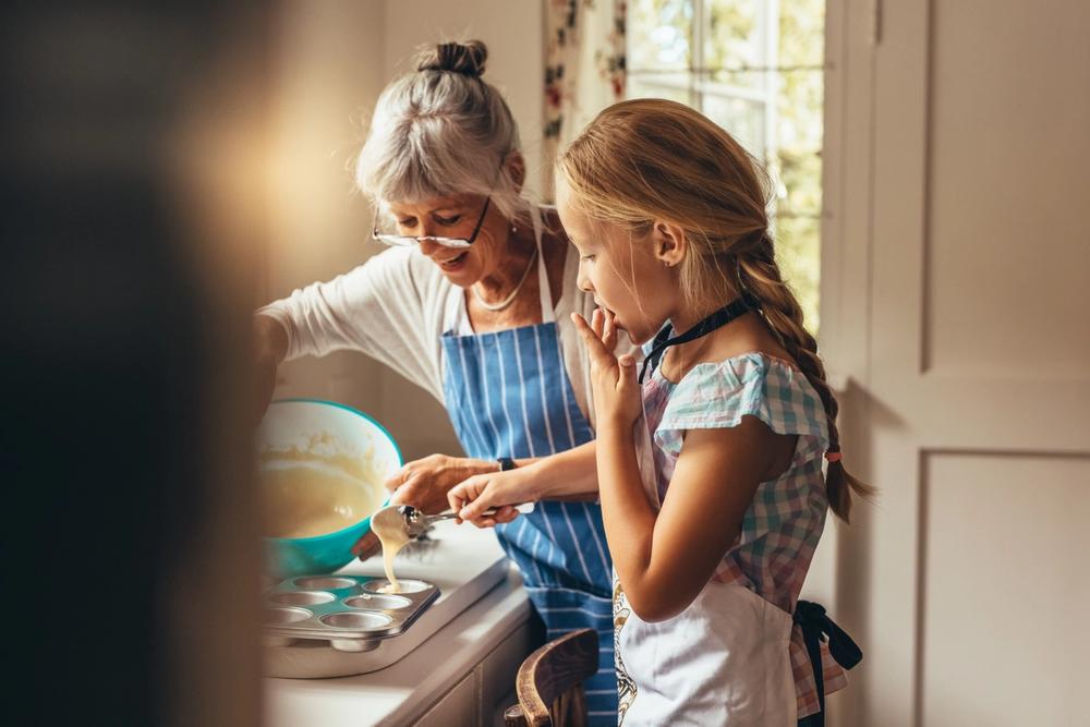Young girl and her Grandma spooning cake mix into baking tins. Young girl and her Grandma spooning cake mix into baking tins.