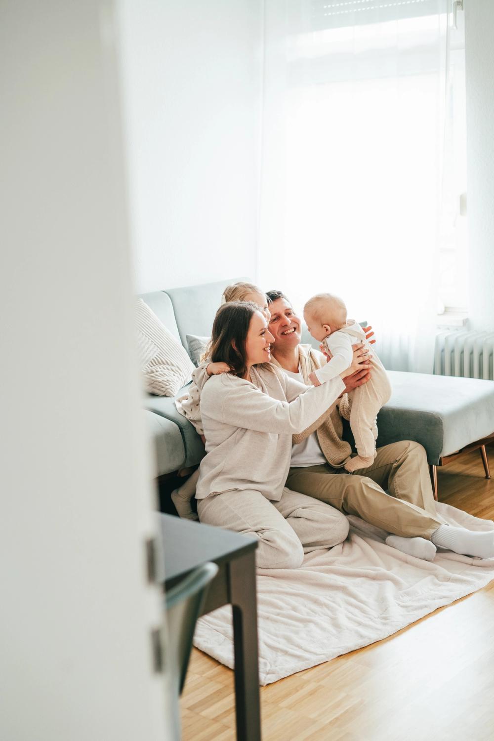 Happy family sitting on the living room floor. Mum holding baby up in the air, everyone looking and smiling. Happy family sitting on the living room floor. Mum holding baby up in the air, everyone looking and smiling.