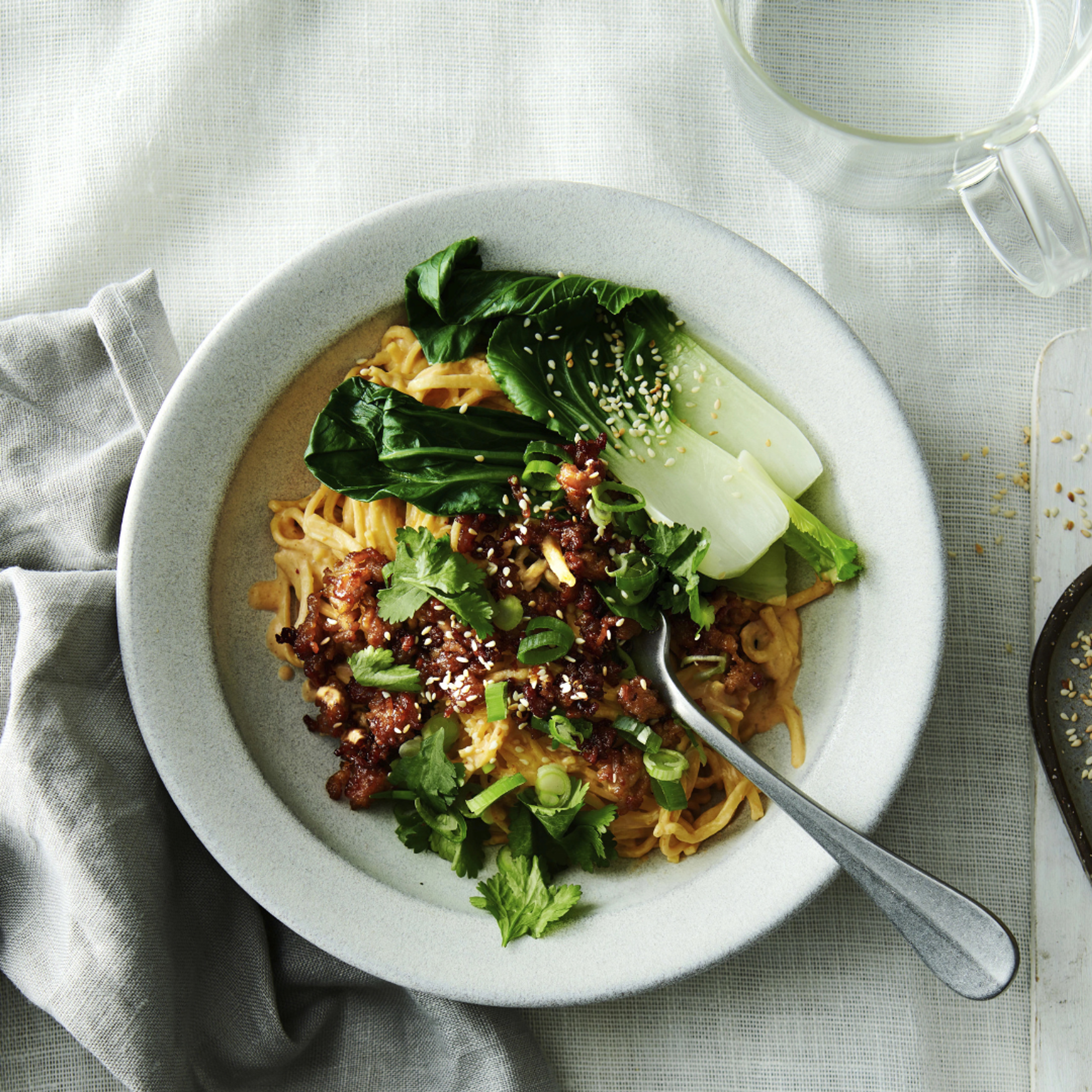 Krämiga nudlar med röd curry toppade med krispig umami-färs, pak choi, koriander, salladslök och sesamfrön serverade i en skål.