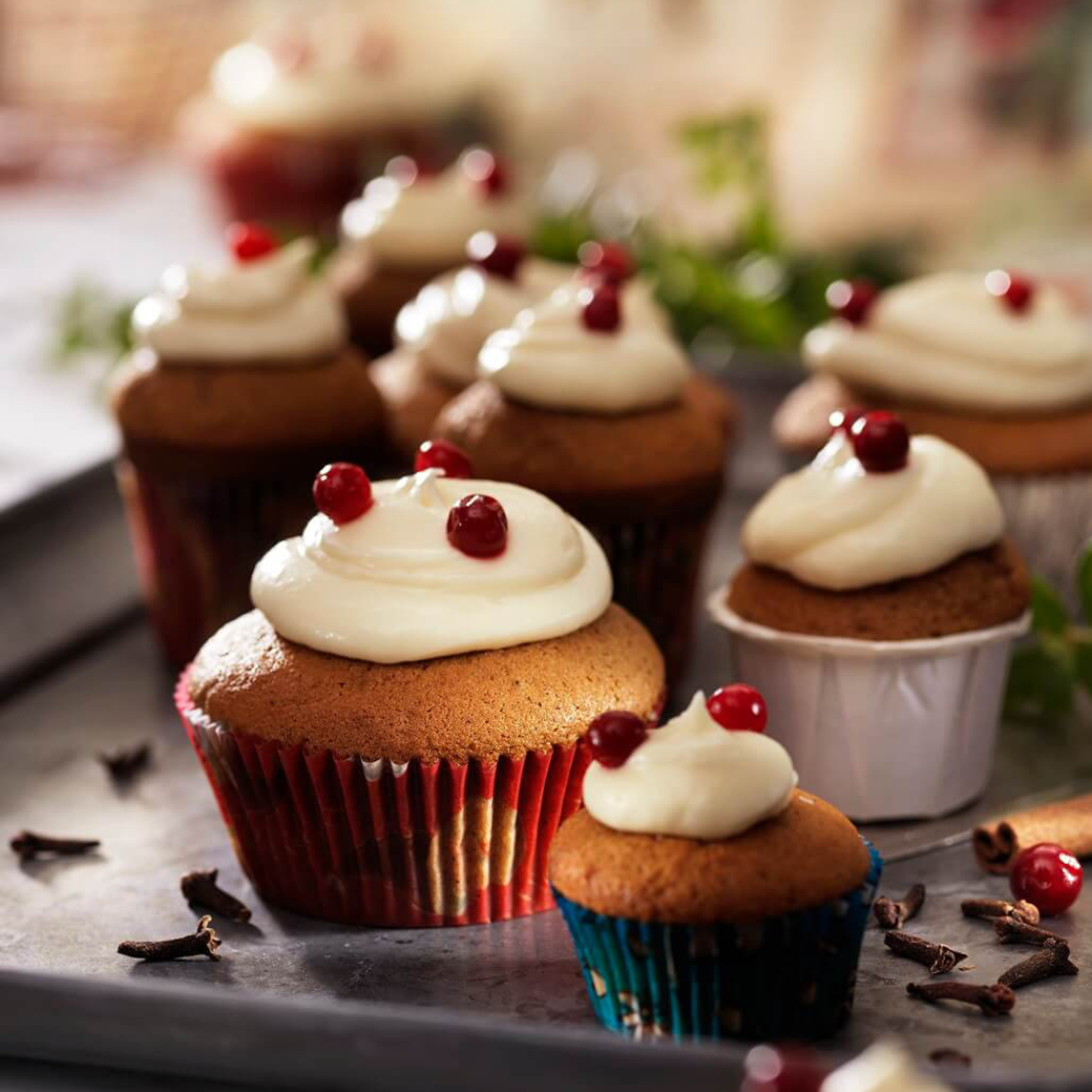 Flera pepparkaksmuffins toppade med frosting och lingon på en bakplåt