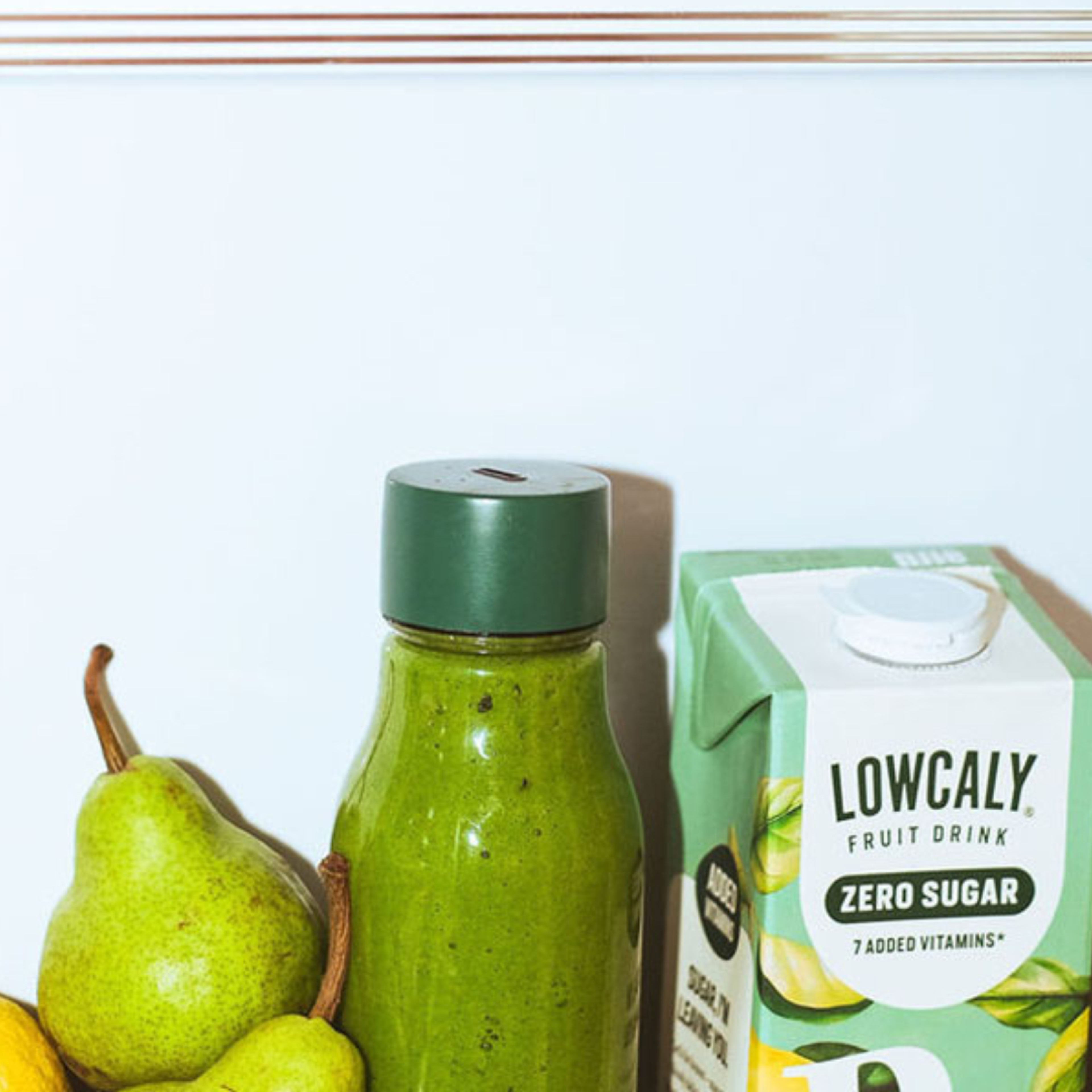 Grön smoothie i flaska bredvid päron och citron, tillsammans med Lowcaly Fruit Drink Zero Sugar med päronsmak.