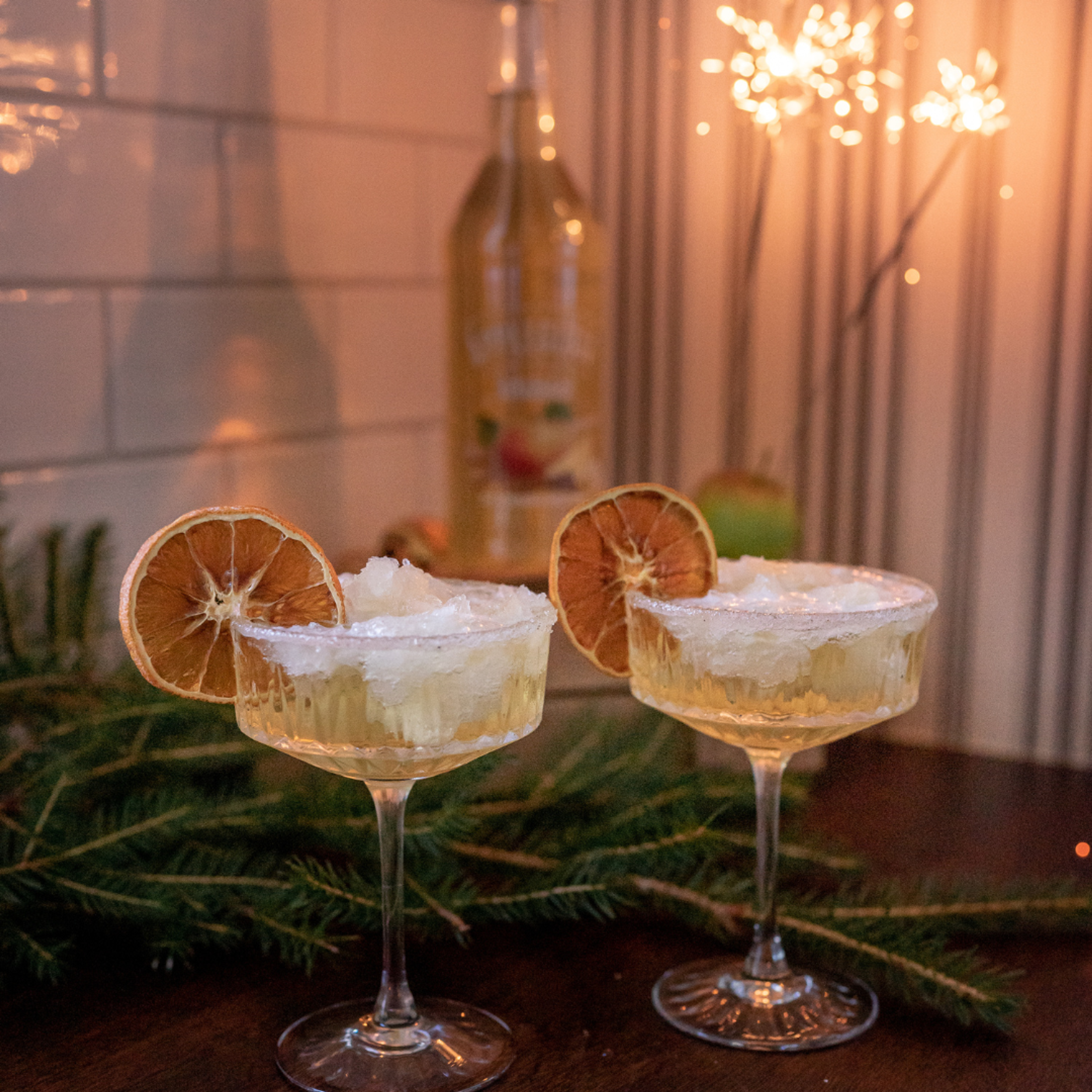 Granité på äppleglögg från Kullamust serverad i cocktailglas med mousserande vin, toppad med is och torkade citronskivor. Julig dekoration och äppleglöggsflaska i bakgrunden.