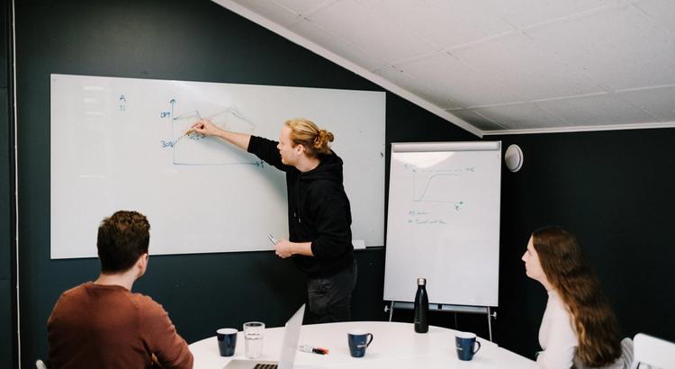 En Deepinsight-ansatt viser frem noe på en whiteboard for to kollegaer.