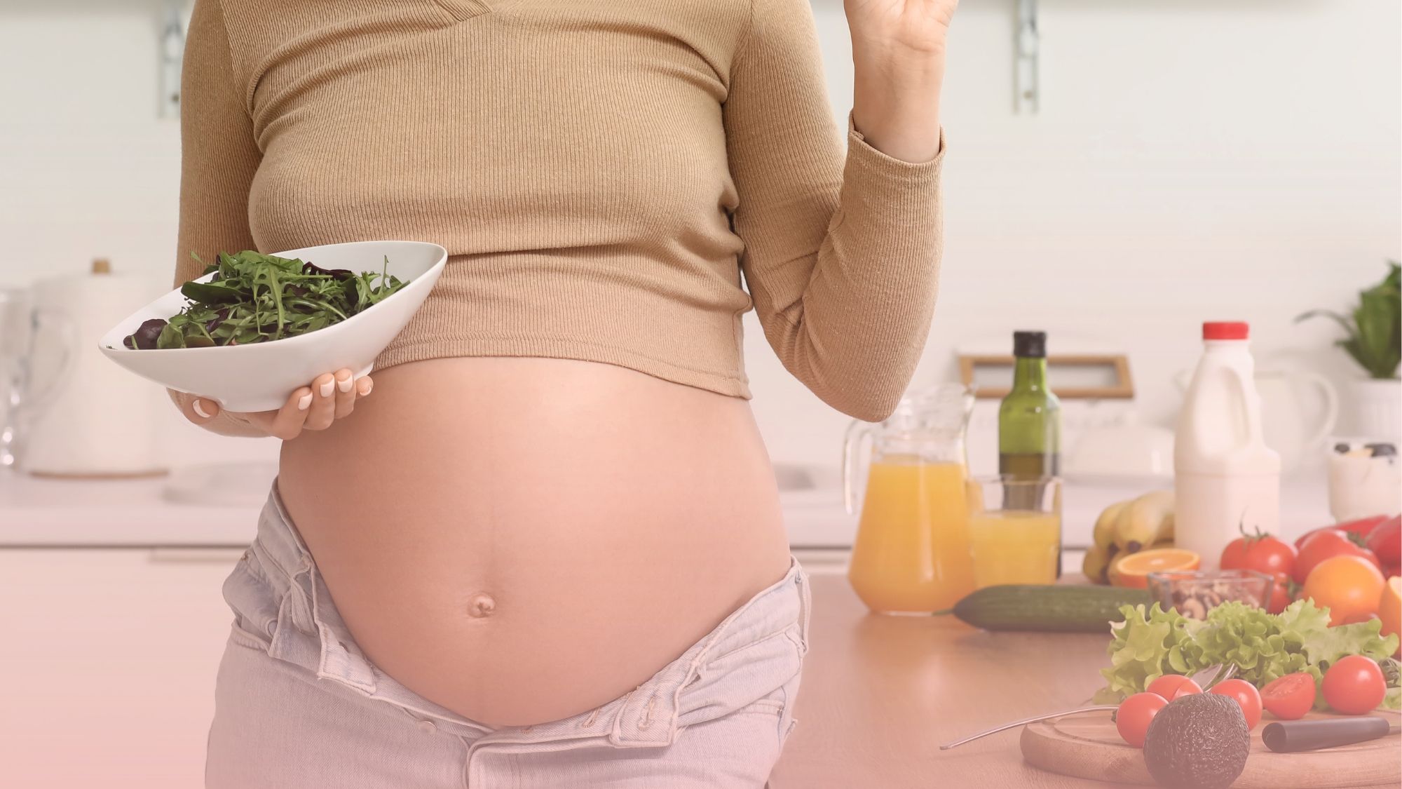 Mujer embarazada sosteniendo un bowl con ensalada saludable en su cocina, reflejando el cuidado de nuestra área de nutrición materno infantil.
