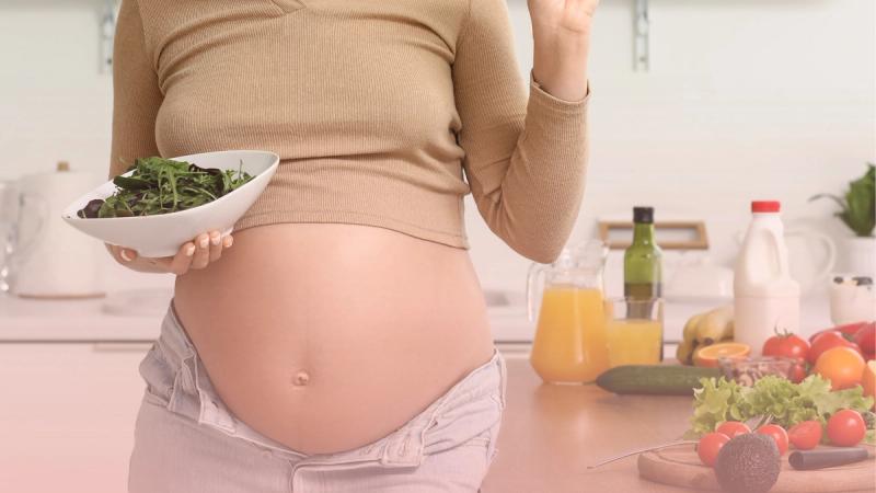 Mujer embarazada sosteniendo un bowl con ensalada saludable en su cocina, reflejando el cuidado de nuestra área de nutrición materno infantil.